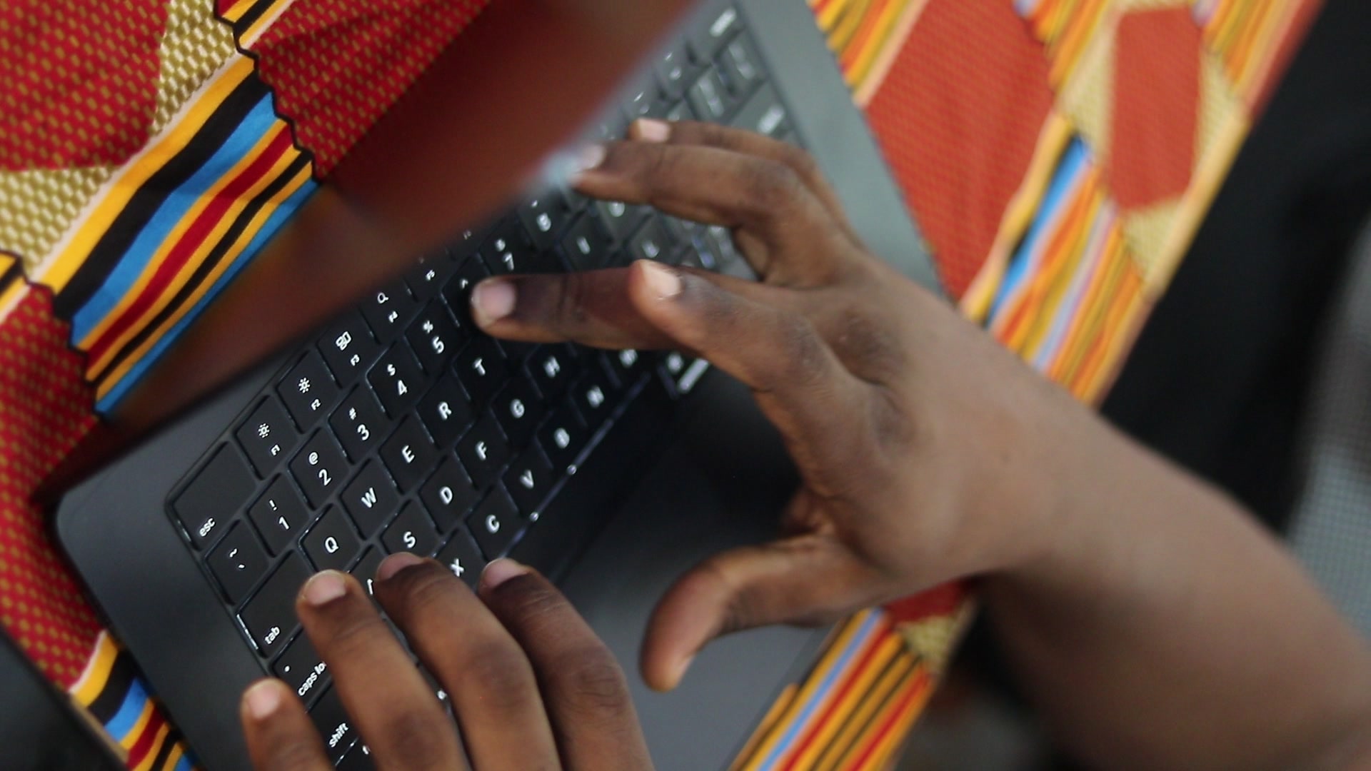 Des mains tapent sur le clavier d’un ordinateur portable posé sur une nappe kente, pendant la première édition.